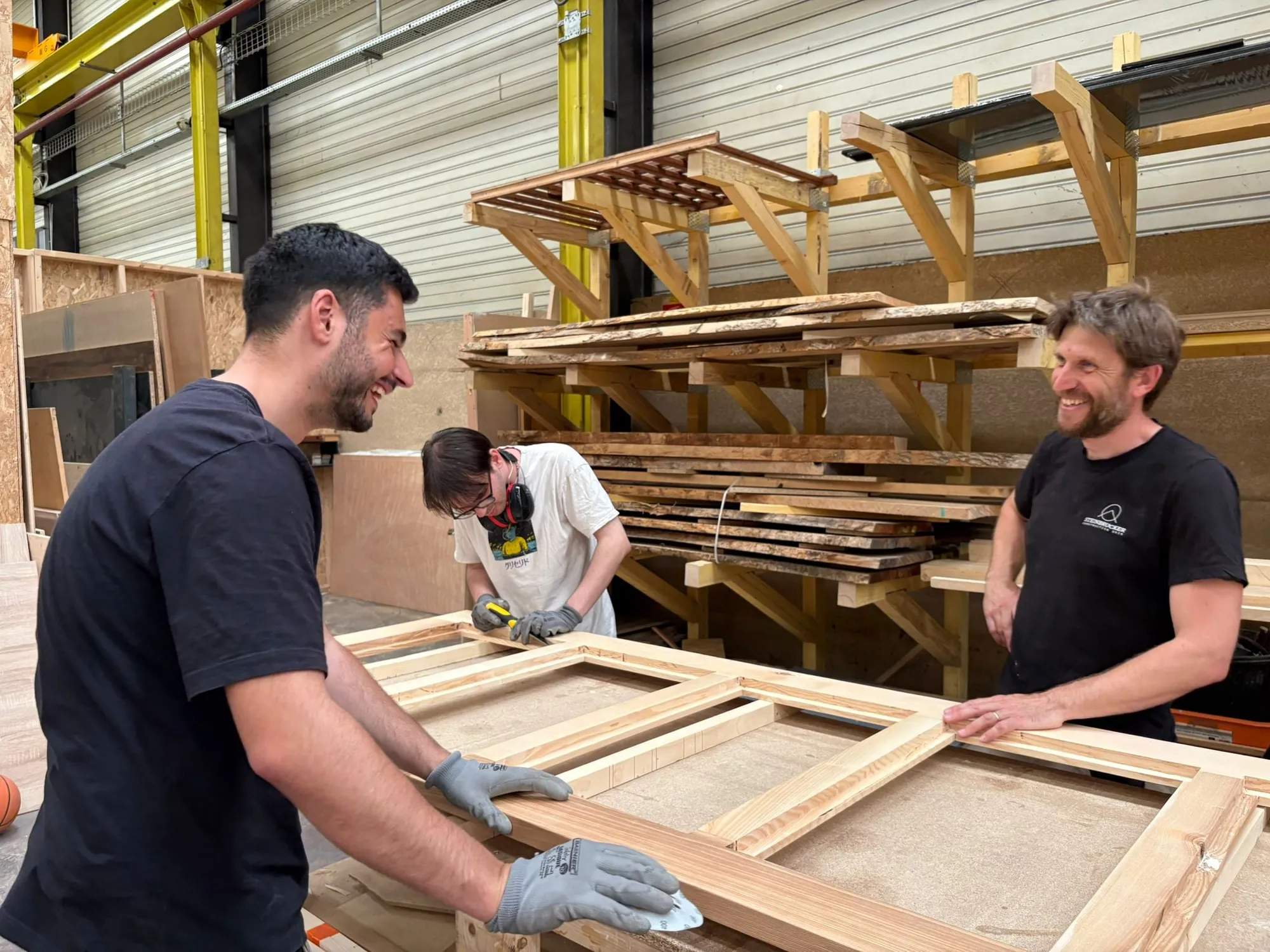 Un membre de l'équipe et le maître menuisier manipulant un cadre en bois à l'atelier