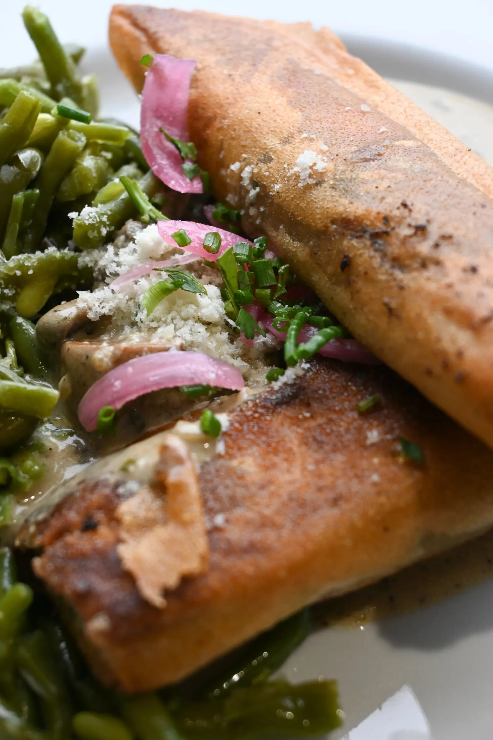 Deux briques croustillantes dorées sur un lit de haricots verts, oignons rouges marinés et sauce crémeuse