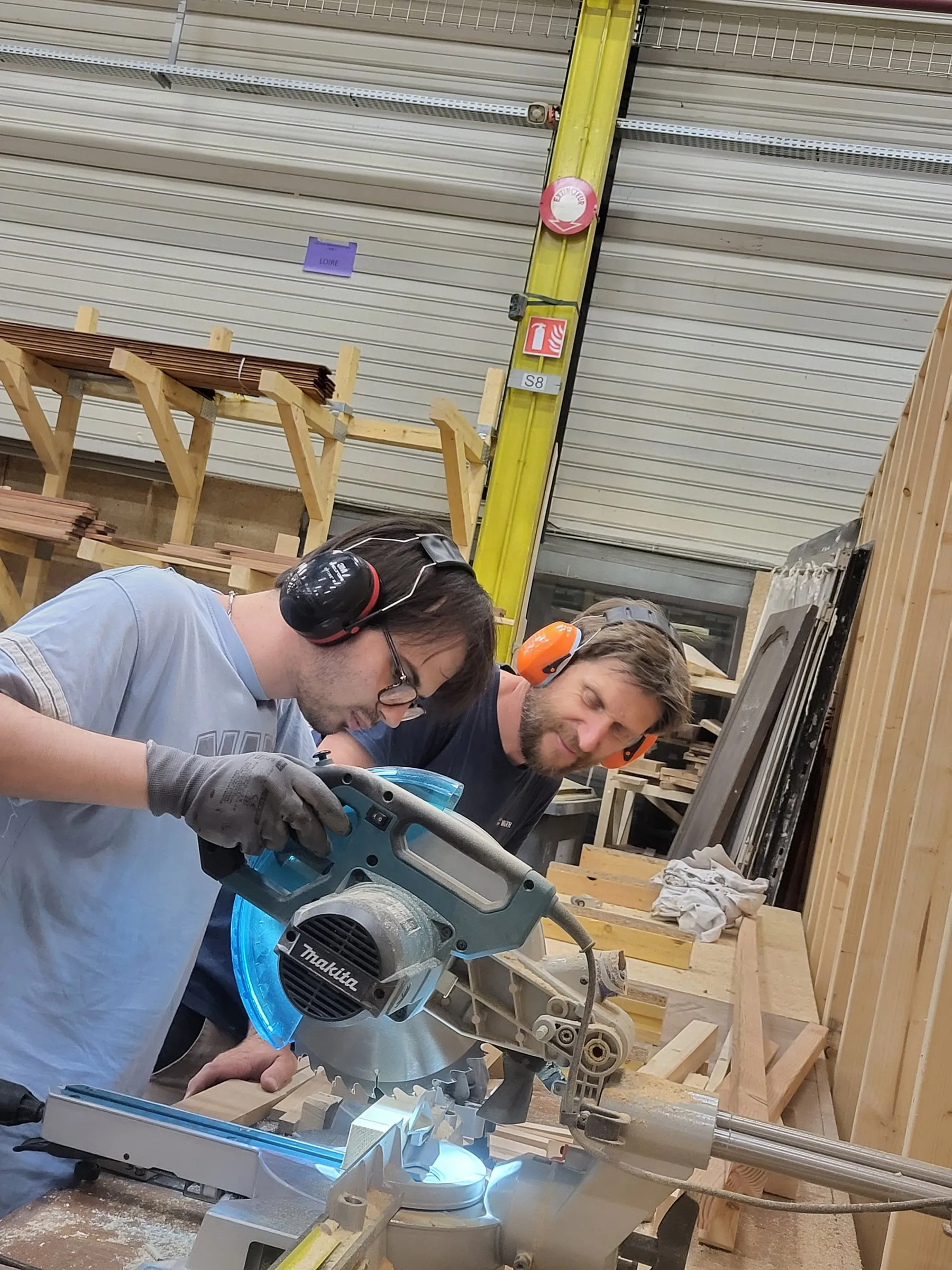 Un apprenti guidé par un professionnel sur une scie à onglet dans l'atelier