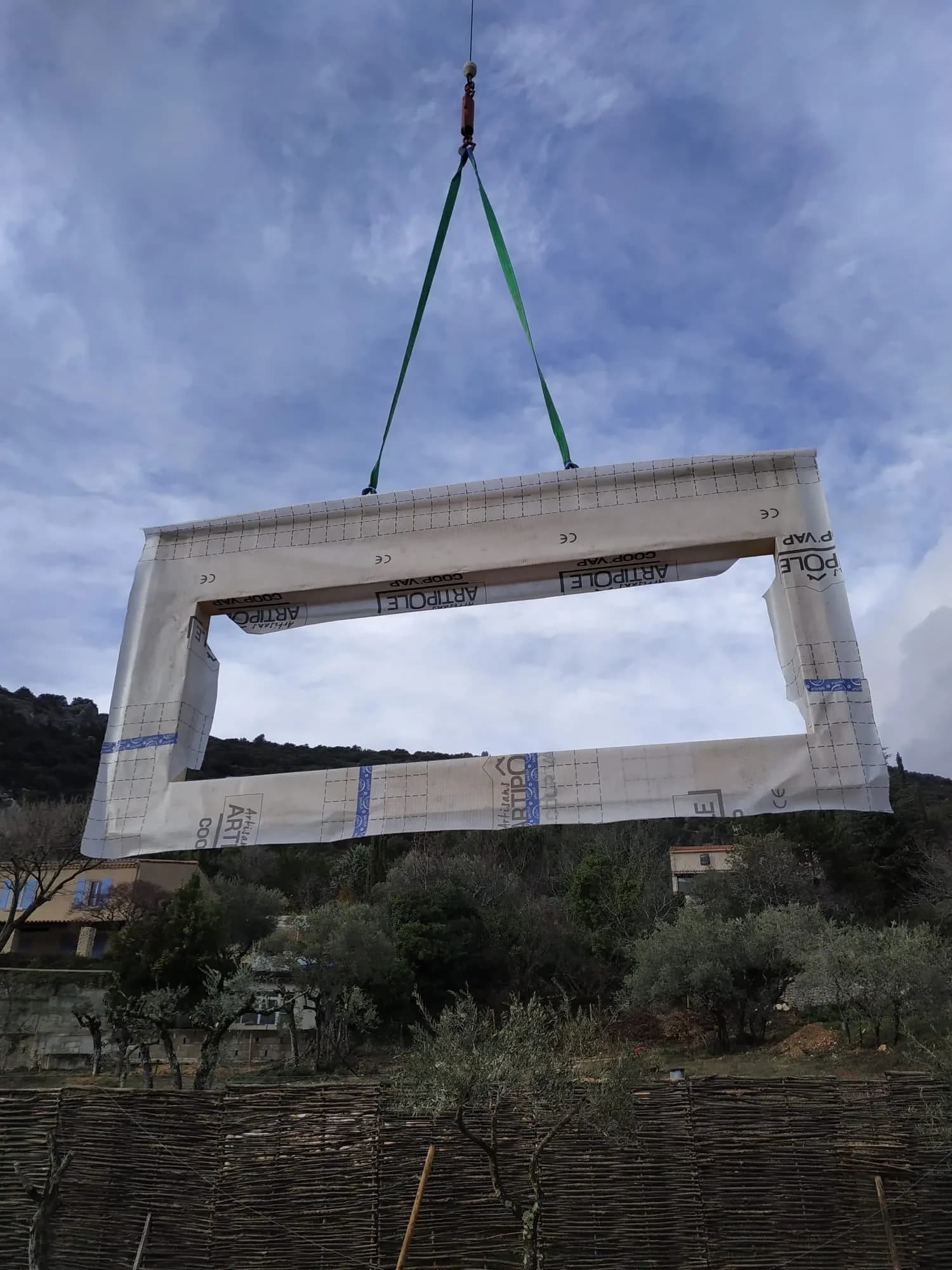 Un pan d'ossature bois soulevé par une grue au-dessus du chantier