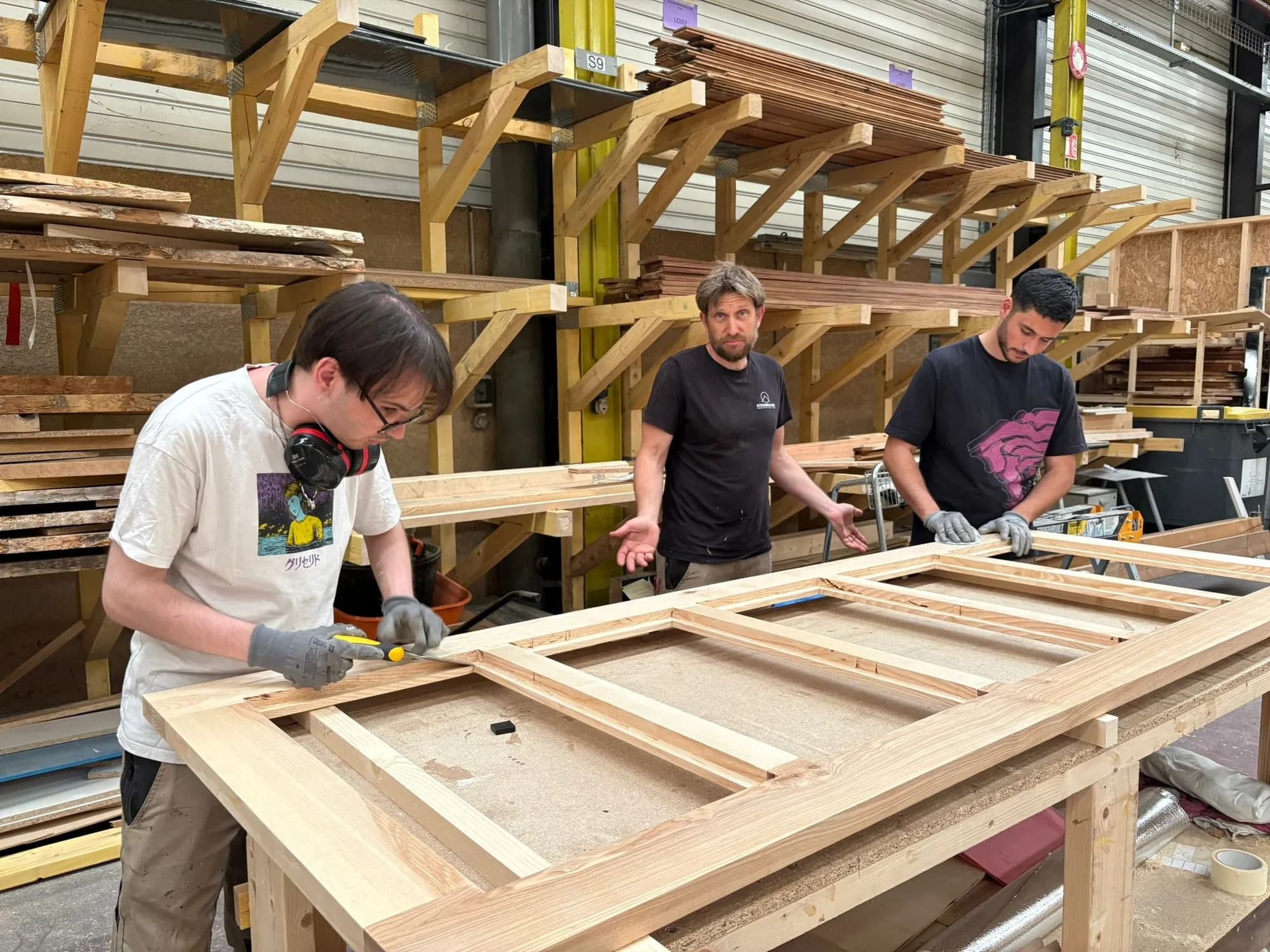 Trois membres de l'atelier assemblent un cadre en bois sur l'établi