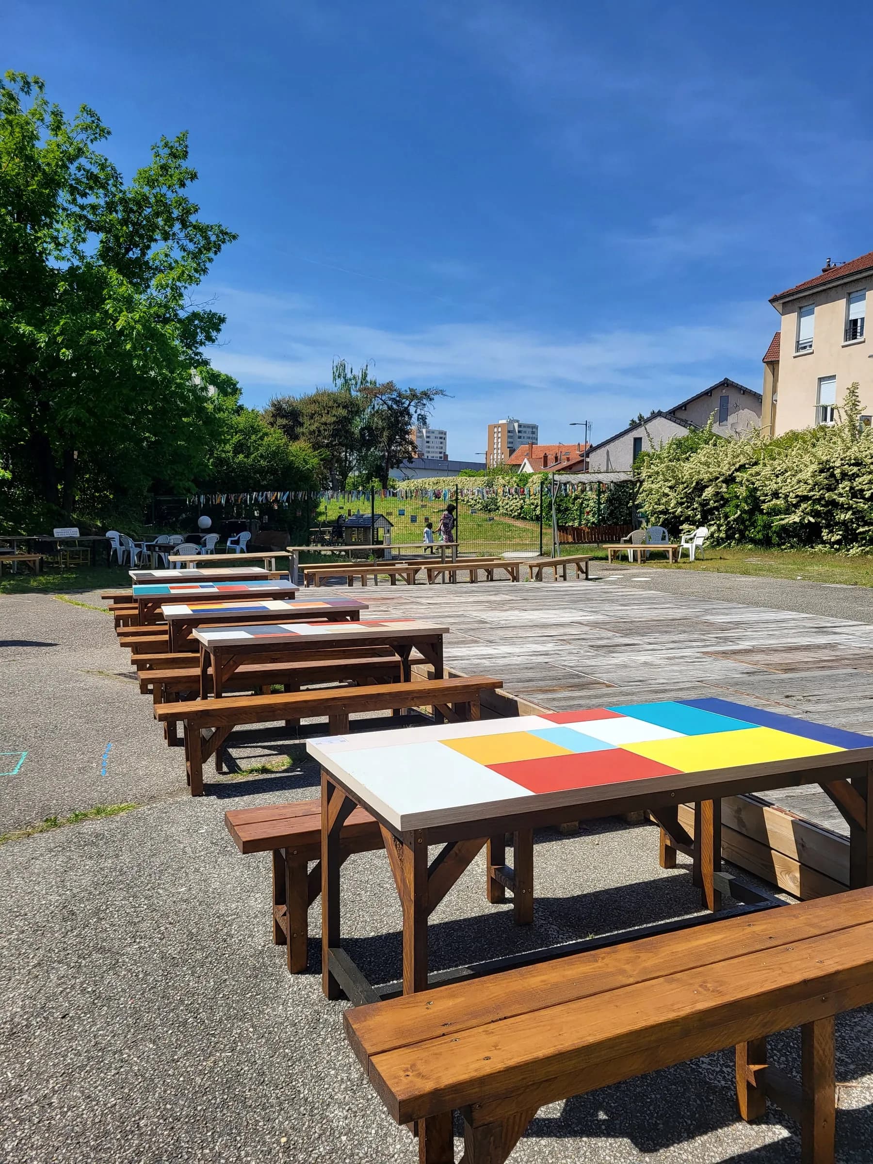 Tables de pique-nique aux plateaux peints de couleurs vives, alignées dans la cour du tiers-lieu